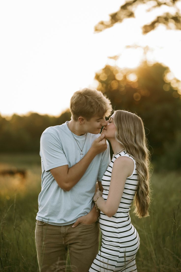 A couple in casual clothing leans against an exposed brick wall while sharing a tender moment together.