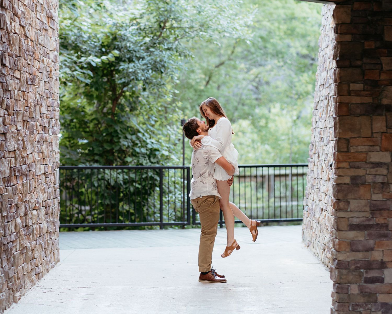 Romantic engagement photos showing a couple embracing near stone pillars, and an arch. Candid documentary West Michigan photographer.