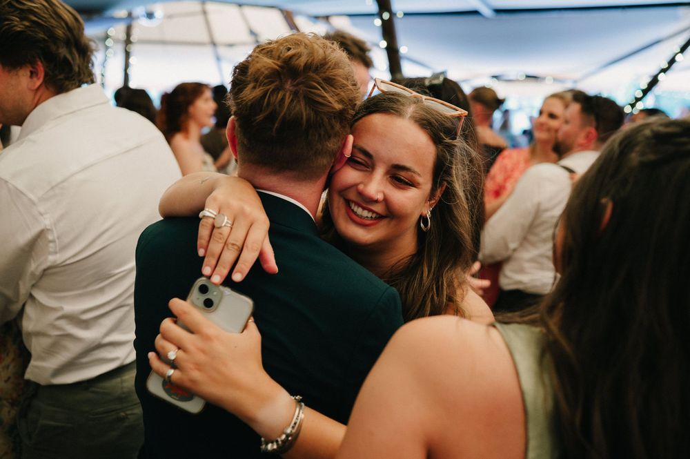 People embracing and hugging during a celebration under a white tent at an outdoor event.
