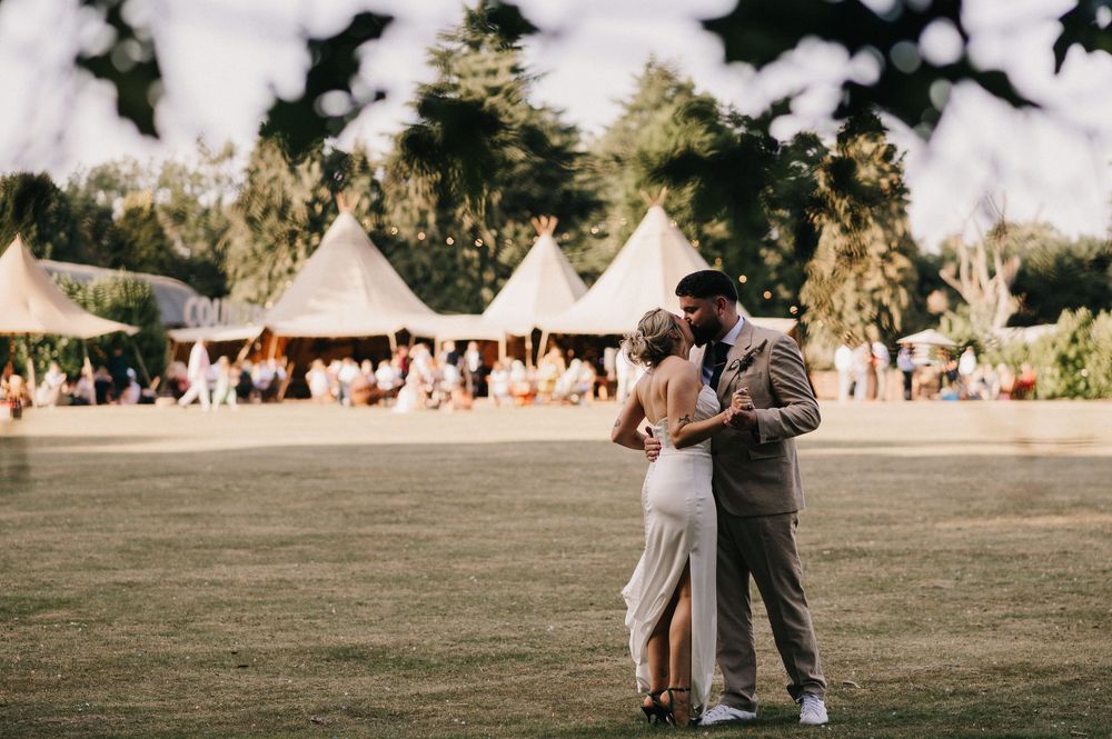 Couple embraces on a lawn at an outdoor wedding reception with white teepee tents in the background.