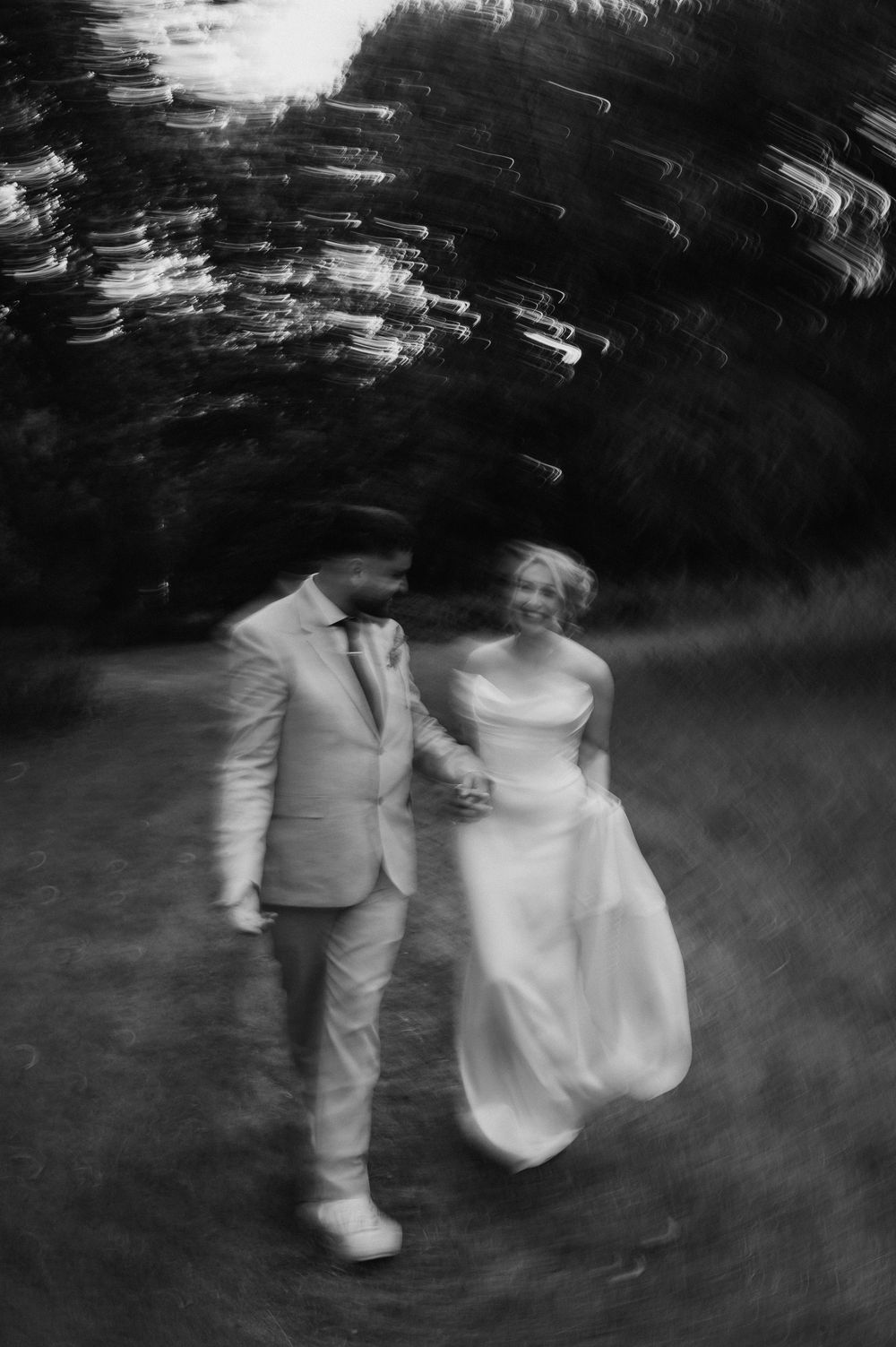 A black and white motion blur photograph shows a couple walking together in formal attire.