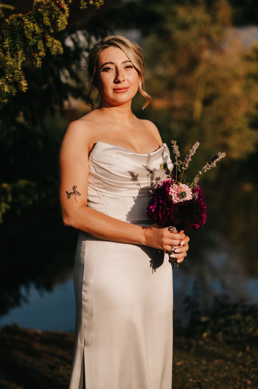 A person in a white wedding dress holds a vibrant purple and burgundy bouquet against a sunset backdrop.