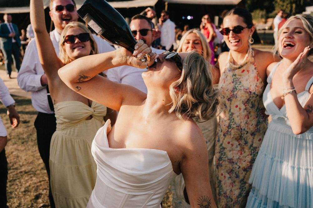 Wedding guests react with excitement and joy during an outdoor celebration in warm sunlight.