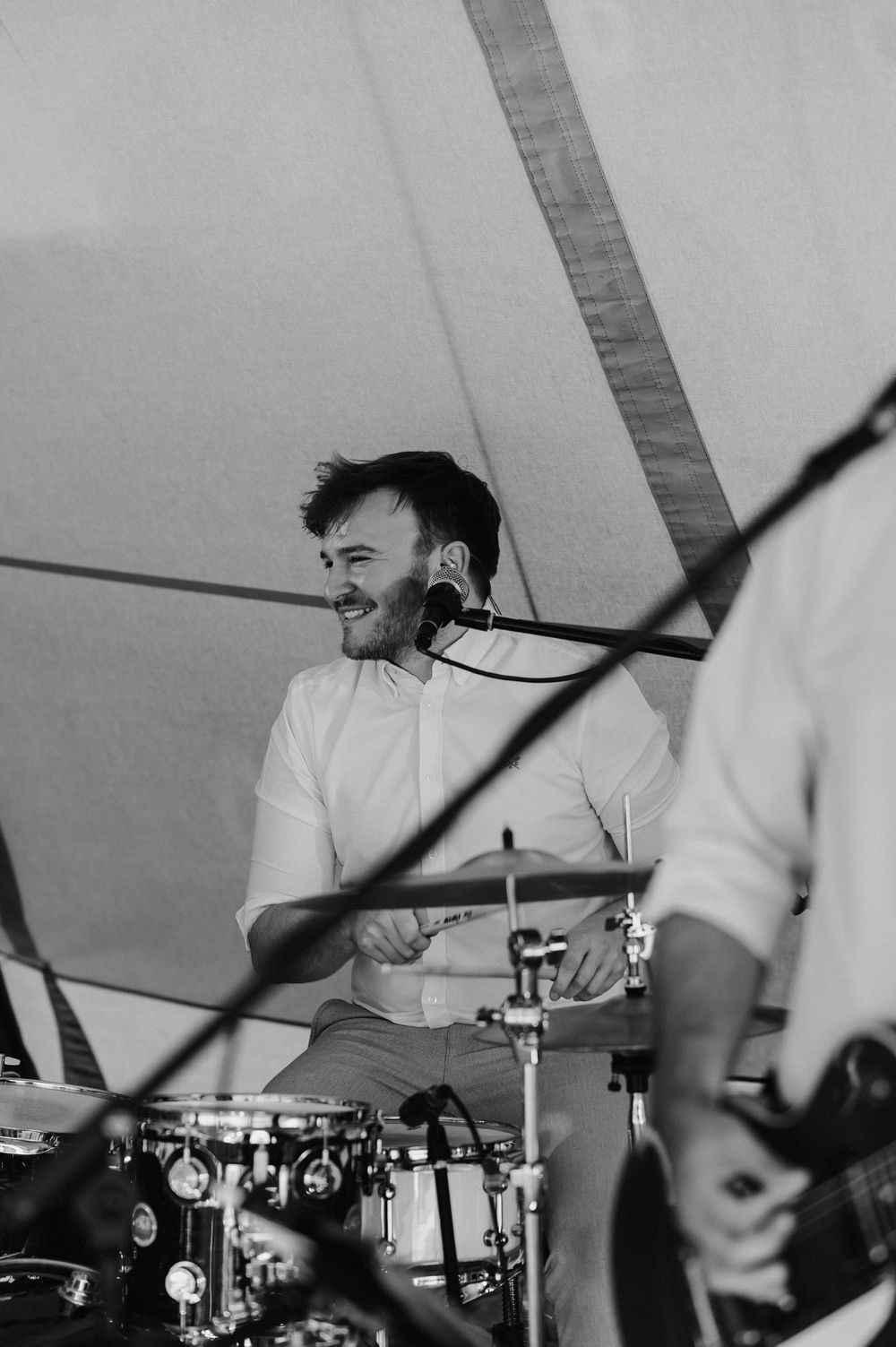 A drummer performs energetically under a white tent at an outdoor event.