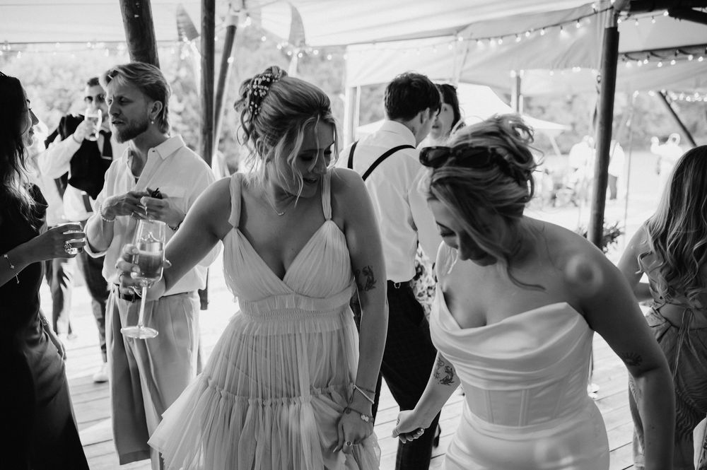 Guests celebrate at a lively outdoor wedding reception under a white tent.