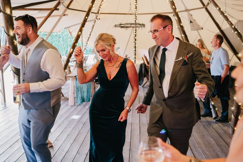 Wedding guests dancing and celebrating together under a tent at an outdoor reception.