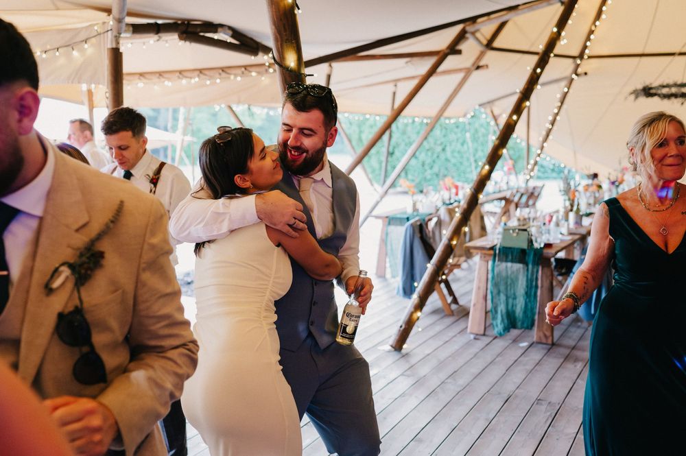 Guests dancing and celebrating together at a wedding reception under a large white tent.