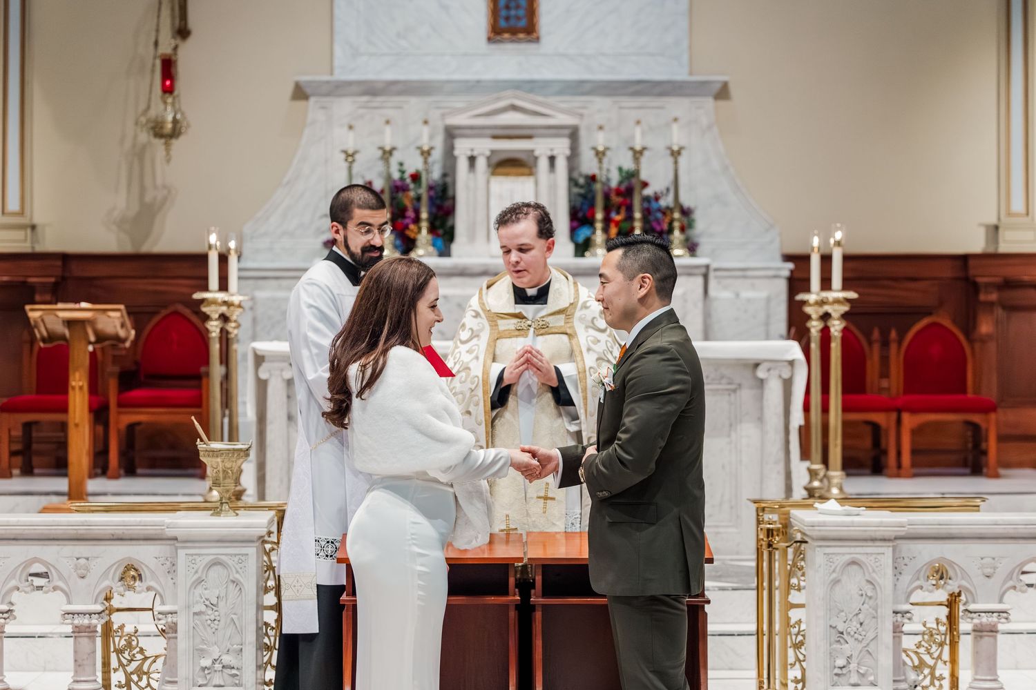 A wedding ceremony taking place in a traditional church with ornate white columns and red carpeting.