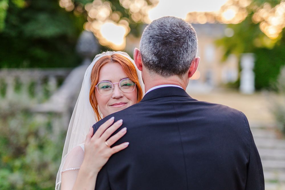 Couple in wedding attire embracing outdoors during golden hour sunset in a garden setting.