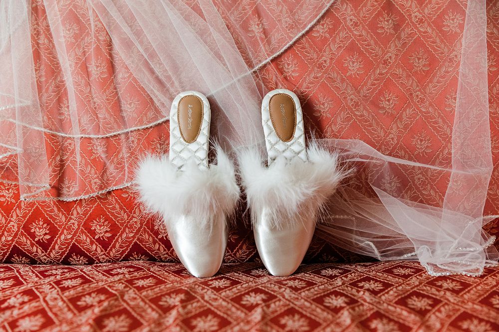Delicate white bridal accessories including shoes and veil arranged on a coral patterned textile.