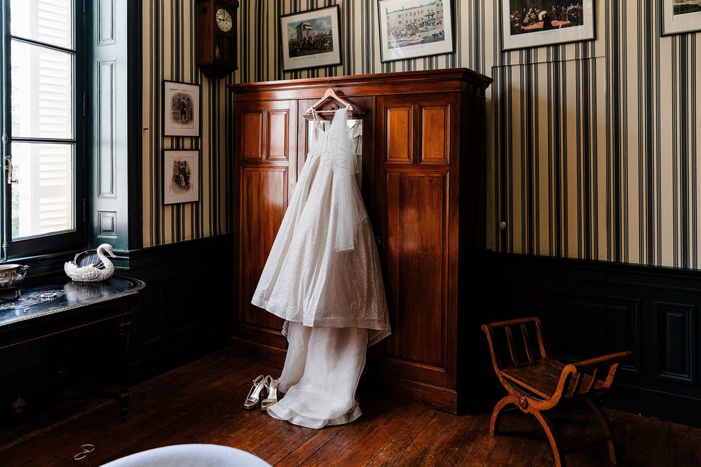 White wedding dress hanging in a vintage room with dark wood paneling and striped wallpaper.