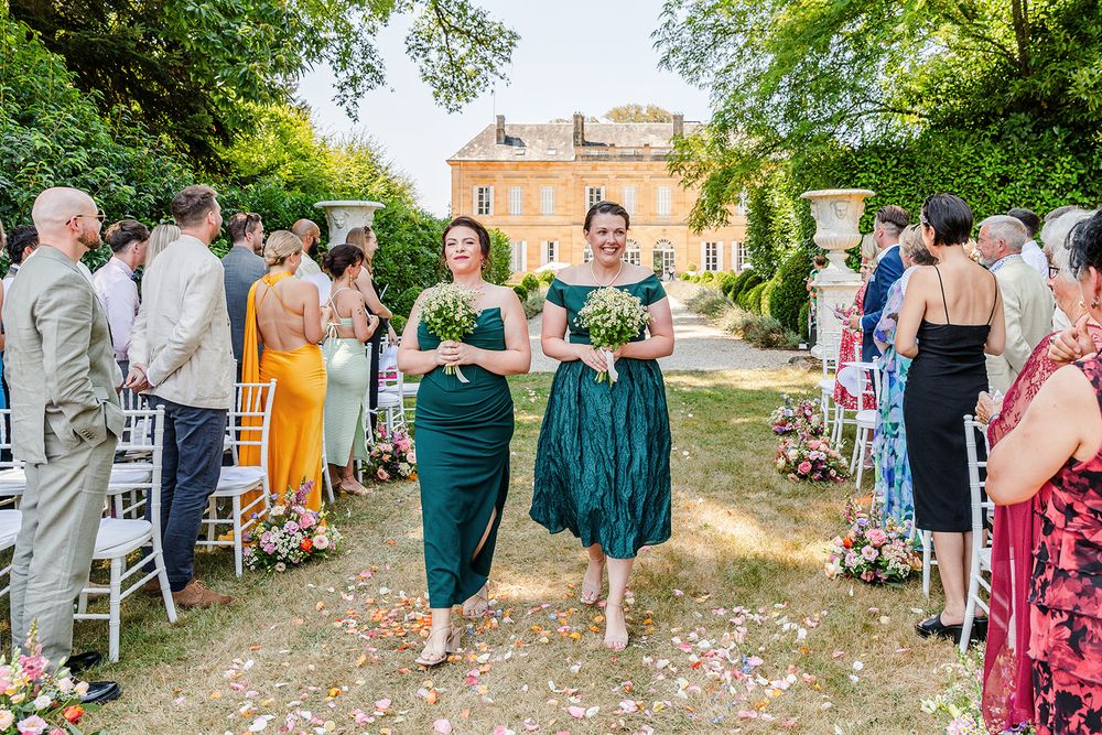 Wedding guests mingle and celebrate on a sunlit lawn with a historic mansion in the background.