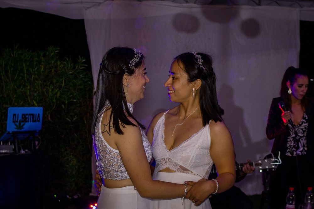Pareja de novias abrazadas bailando en la fiesta de su matrimonio iluminación nocturna y ambiente festivo con DJ de fondo