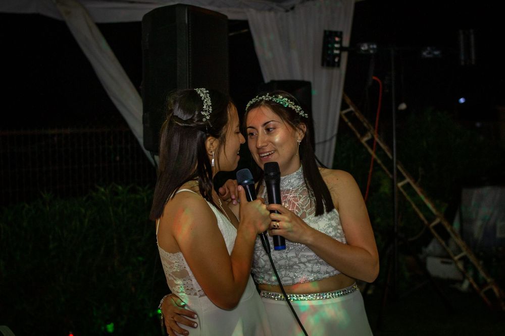Novias celebrando su boda cantando con micrófonos durante la fiesta nocturna, luciendo vestidos blancos con detalles de encaje y brillo.