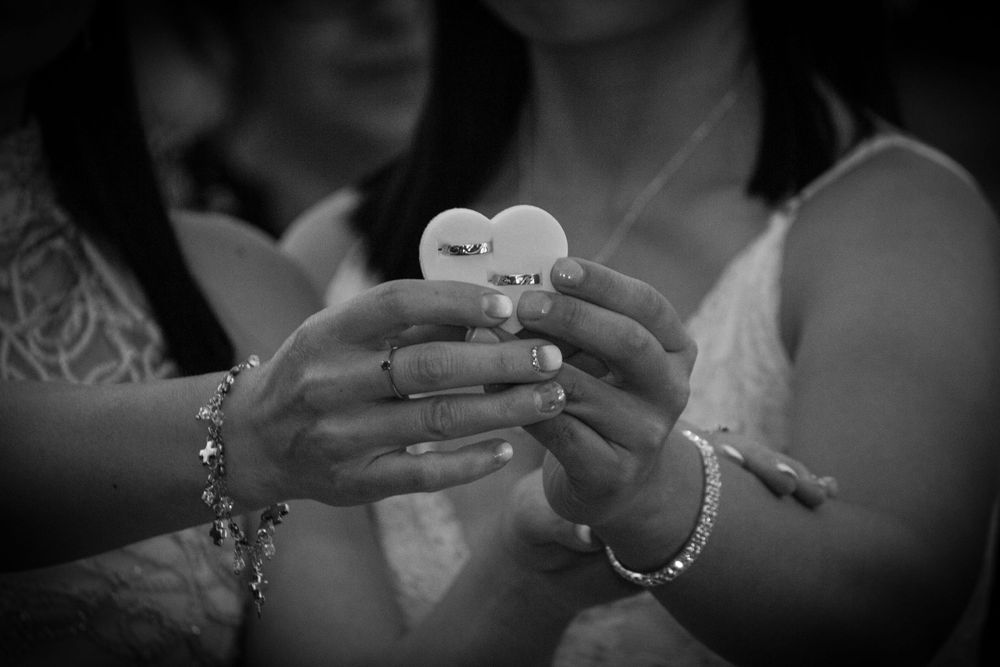 Manos de las novias sosteniendo un porta alianzas en forma de corazón con sus anillos de matrimonio fotografía en blanco y negro.