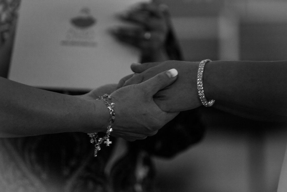 Primer plano artístico en blanco y negro de manos de novias entrelazadas se aprecian pulseras de plata y detalles de manicura