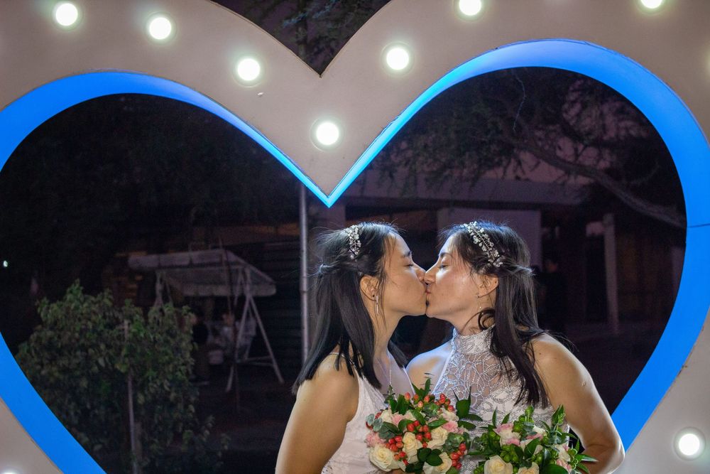 Primer plano de novias besándose bajo un arco de corazón con luces LED azules y blancas en una celebración de boda al aire libre