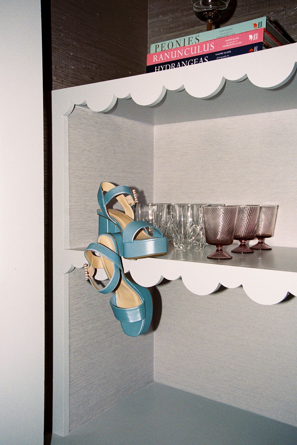 Blue platform sandals displayed on white floating shelves with glassware and books.