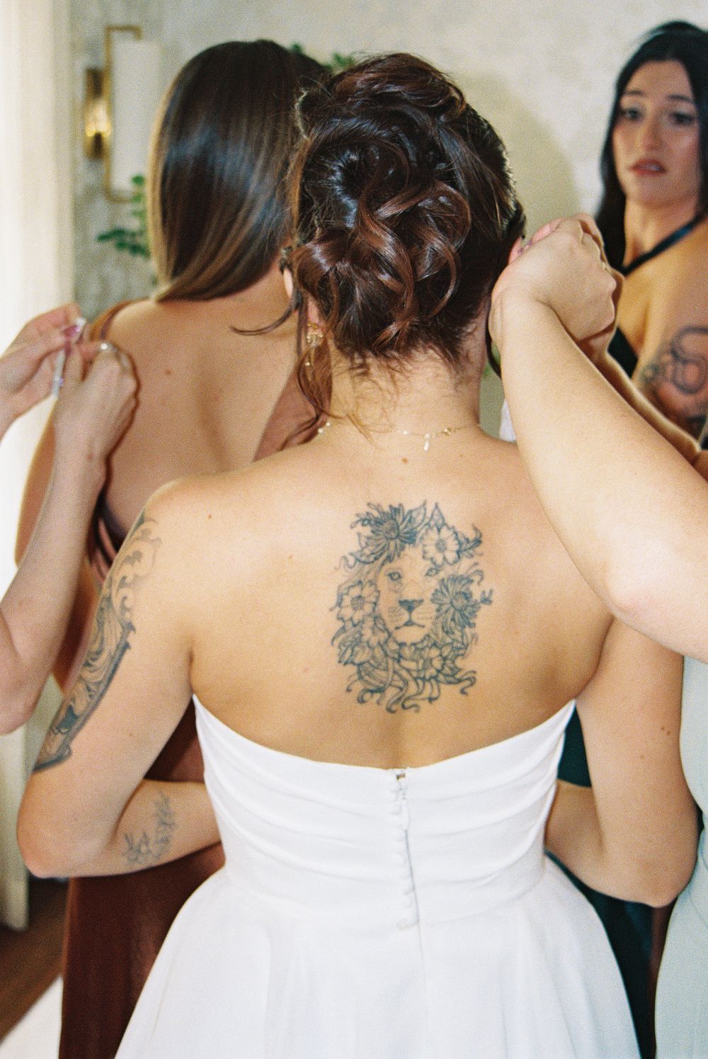 Back view of bridesmaids showing ornate tattoo designs through white dresses.