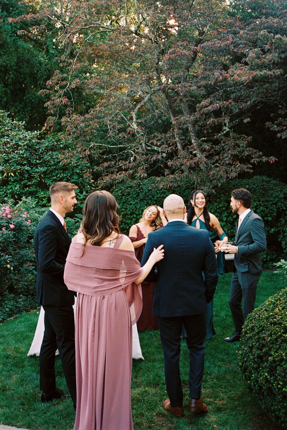 Wedding guests mingle and socialize in an outdoor garden setting during cocktail hour.