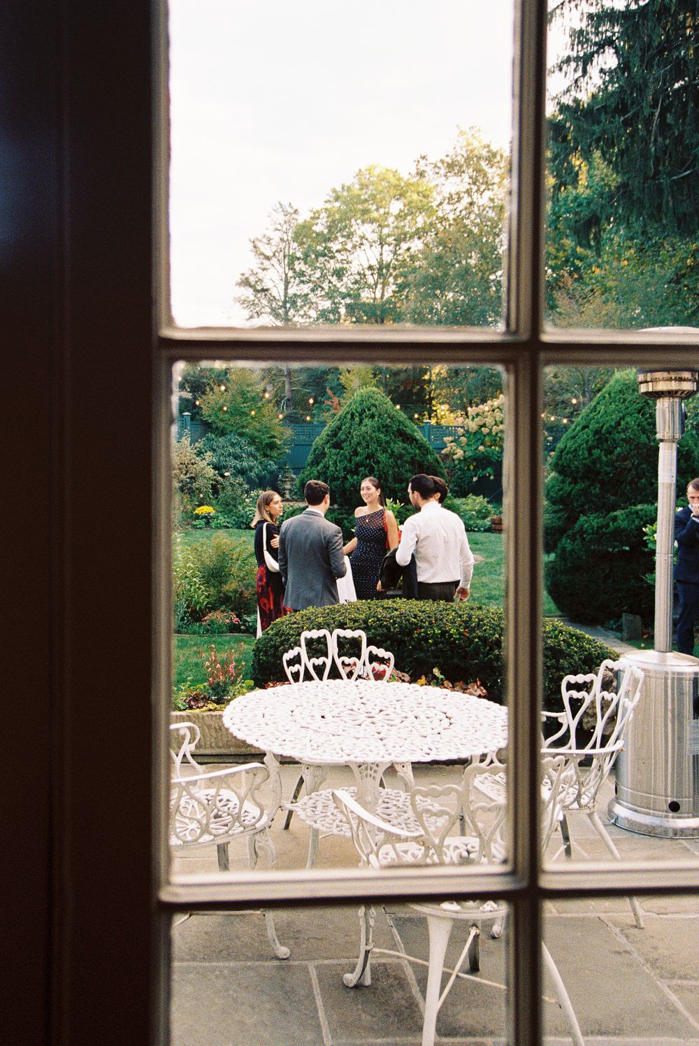 White wrought iron patio furniture arranged on an outdoor terrace with garden views through large windows.