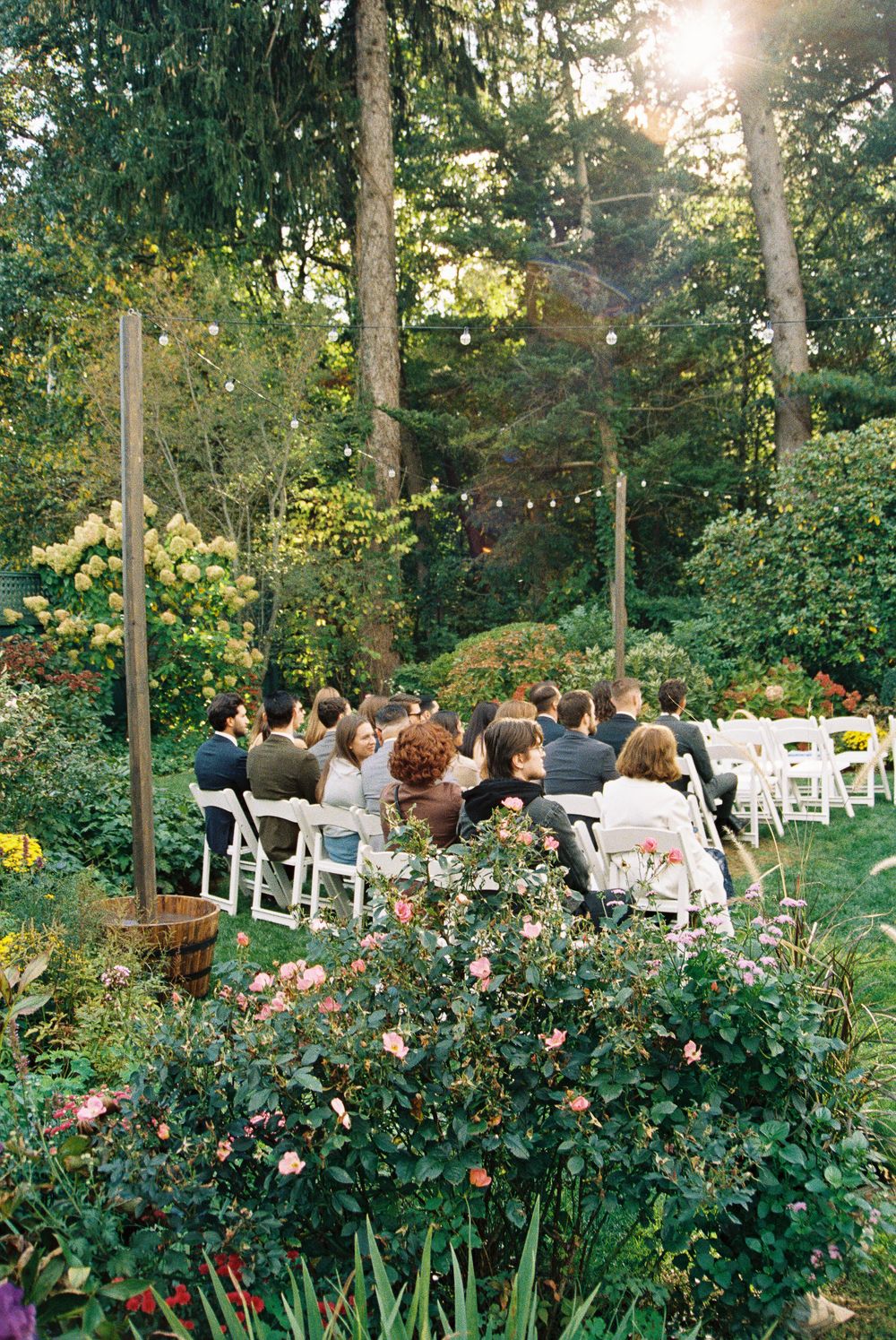 Garden wedding ceremony setup with white chairs and floral arrangements in a sunlit outdoor setting.