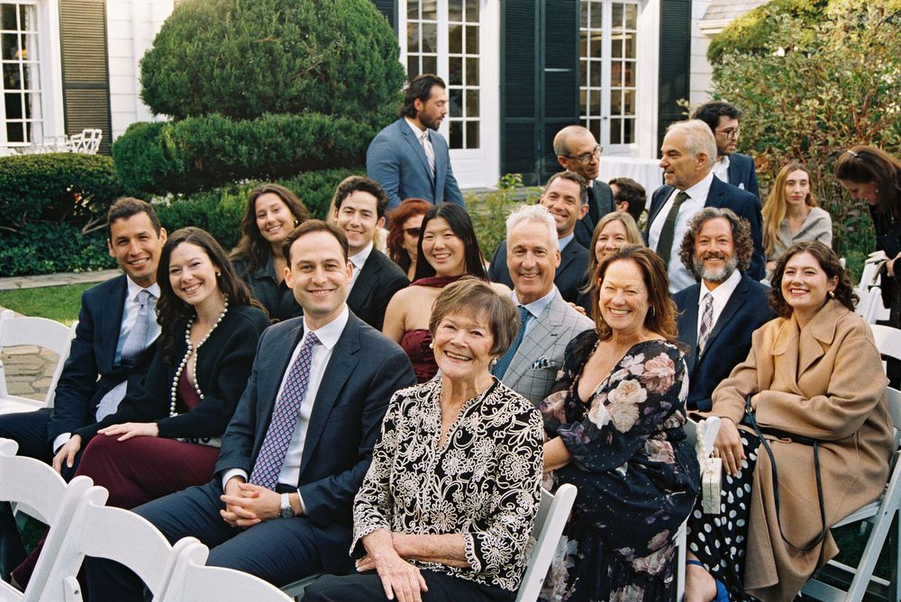 A group of formally dressed people gather outdoors for a social event on a sunny day.