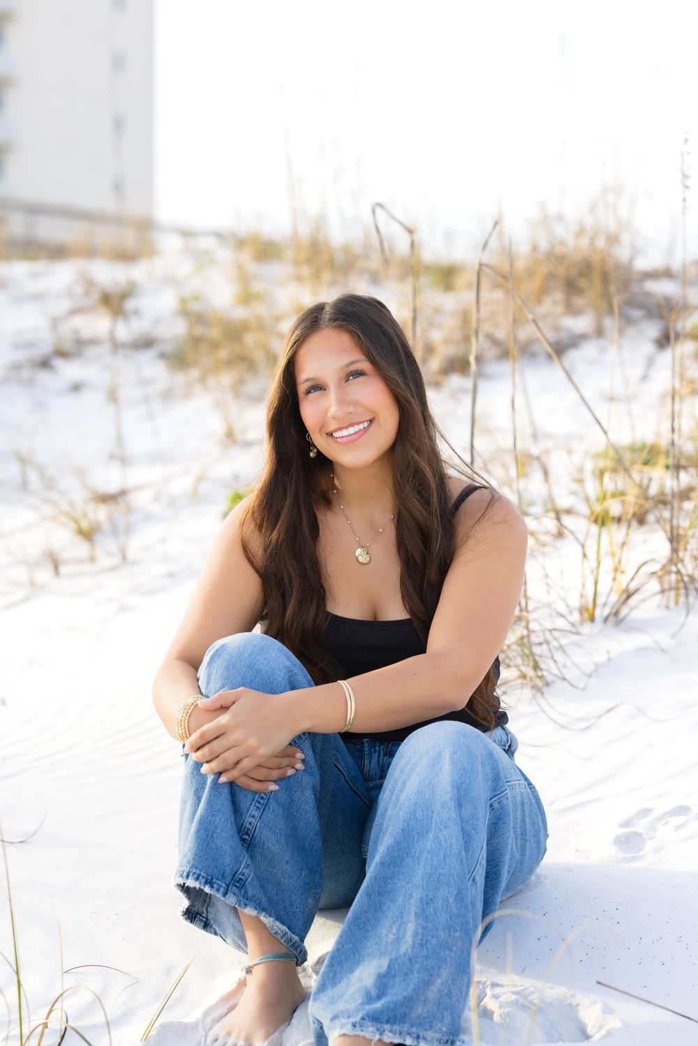 Person in blue jeans sits casually on white sand beach during a sunny outdoor portrait photography session.