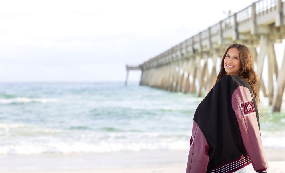 Person wrapped in a black blanket stands by a wooden pier on a cloudy beach day.