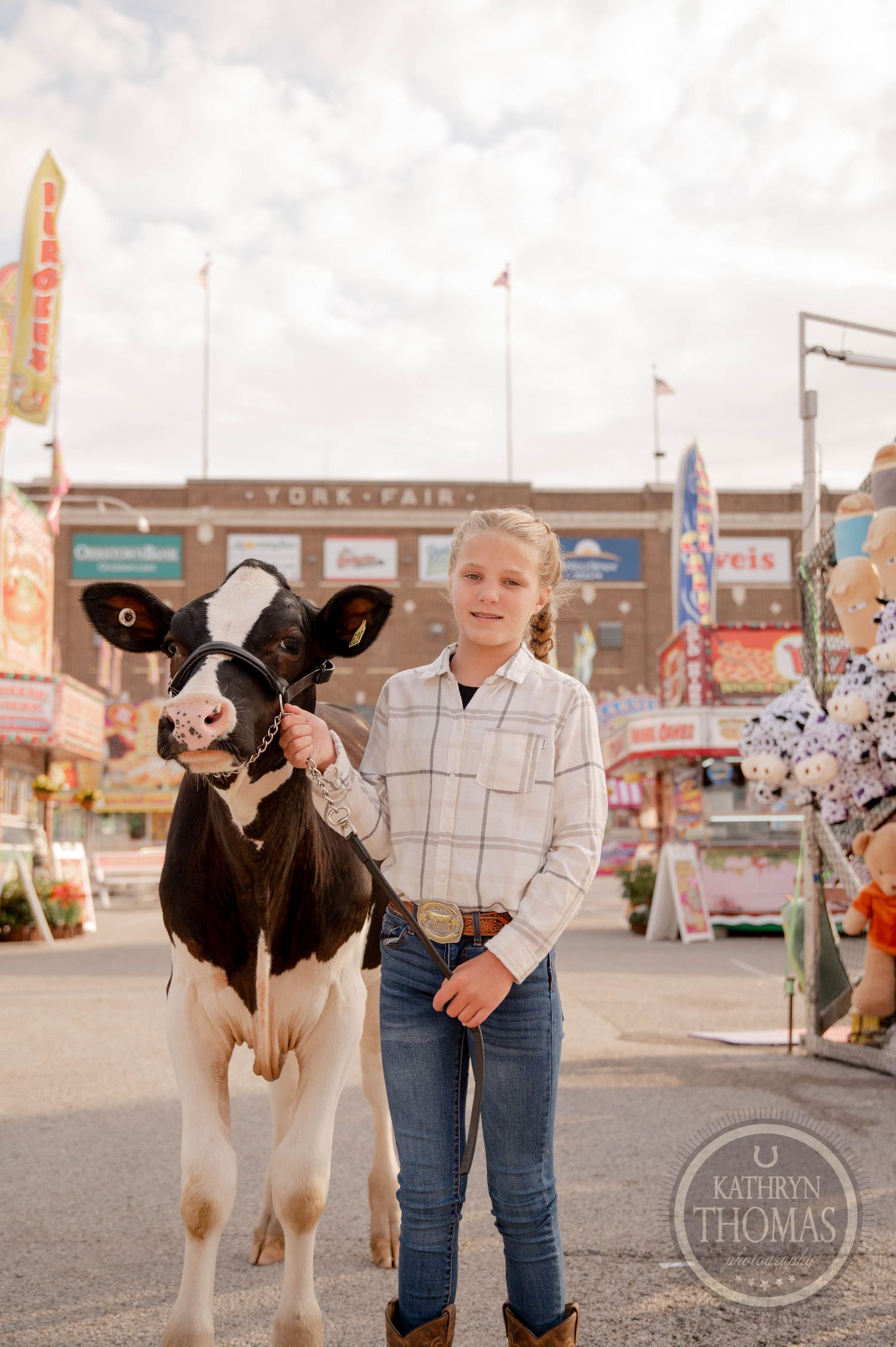 Young girl in flannel shirt and jeans holds a black and white calf at the York Fair fairgrounds.