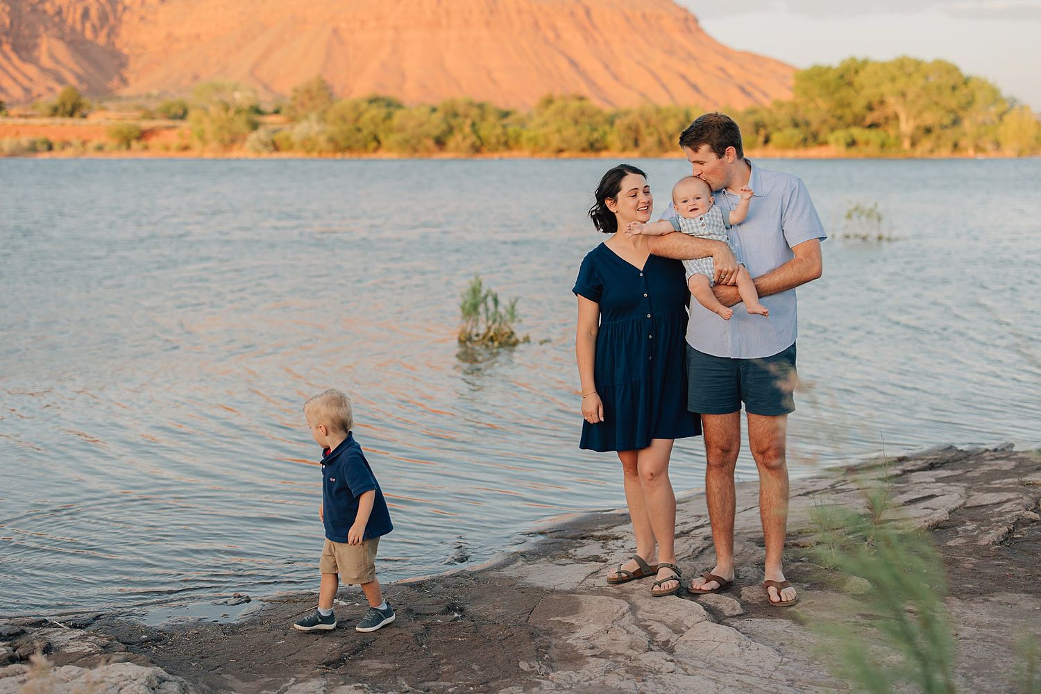 Family of four enjoying a scenic lakeside sunset with red rock mountains in the background.