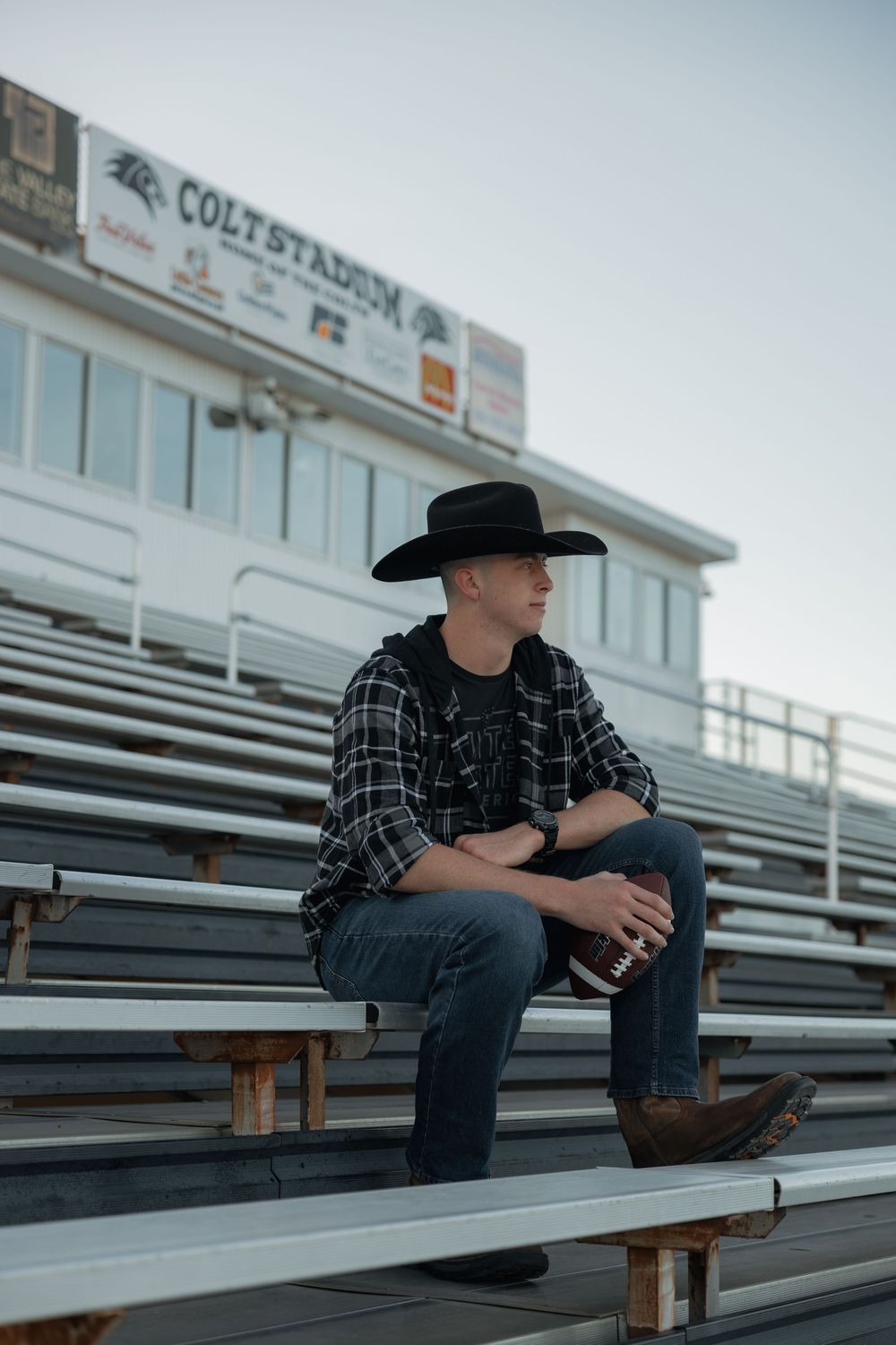 Young man in black cowboy hat and plaid shirt sitting on bleachers at Colt Stadium.