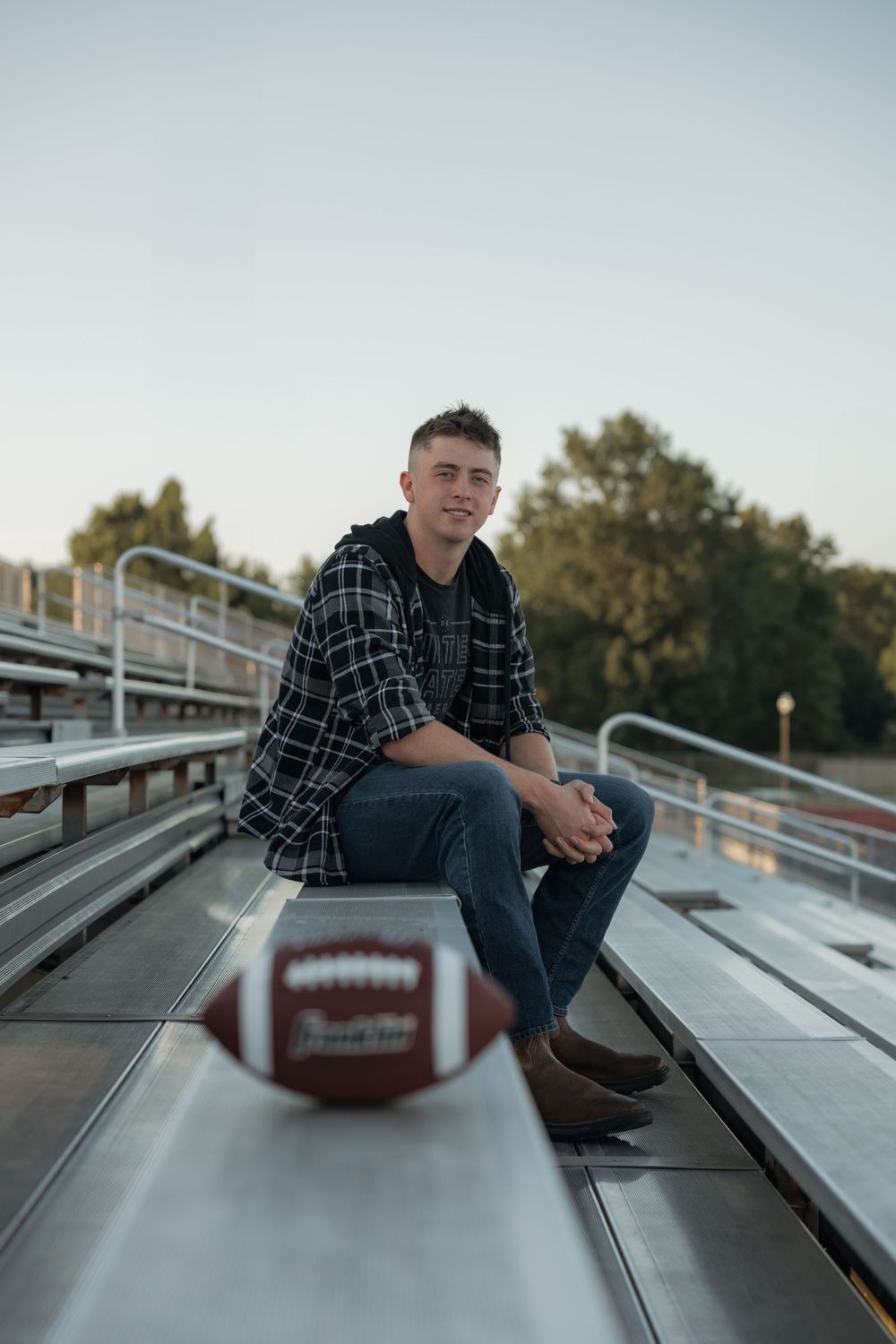 Smiling young man in plaid shirt sitting on bleachers with Franklin football in foreground.