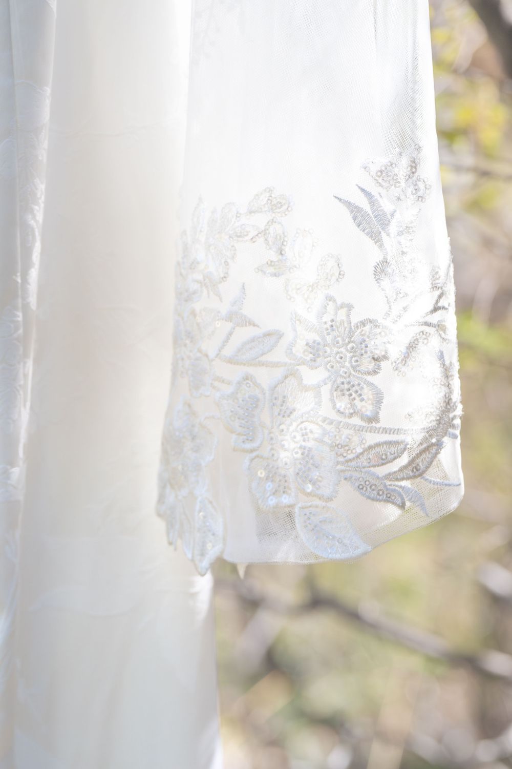 Close-up of a white wedding dress hem with delicate silver floral embroidery details.