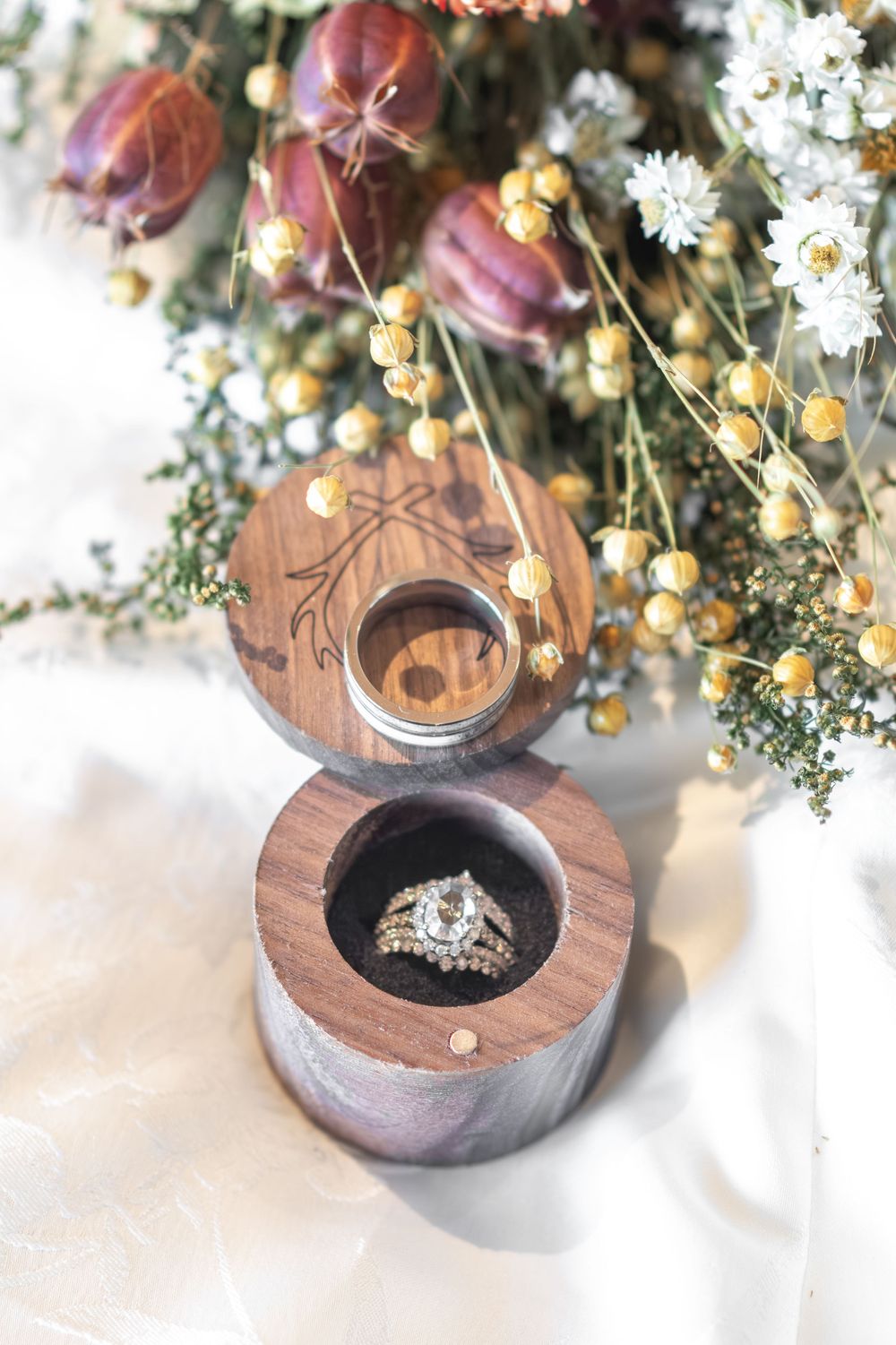 Diamond engagement ring and wedding band displayed in a wooden ring box with dried florals.
