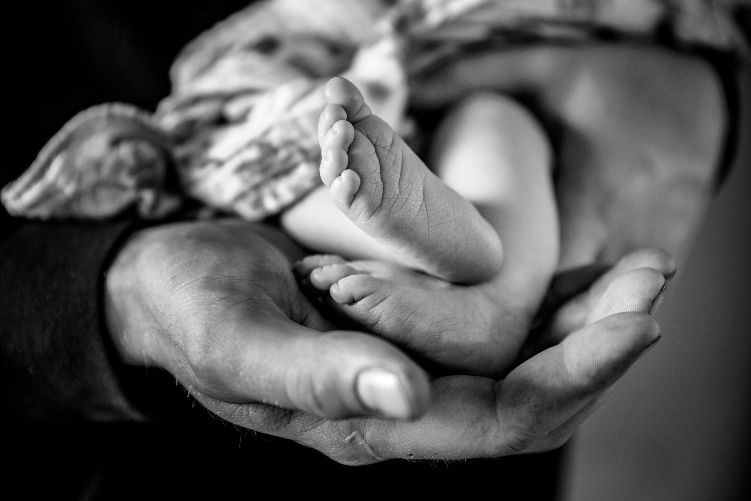 Black and white photo of newborn baby feet cradled gently in adult hands.