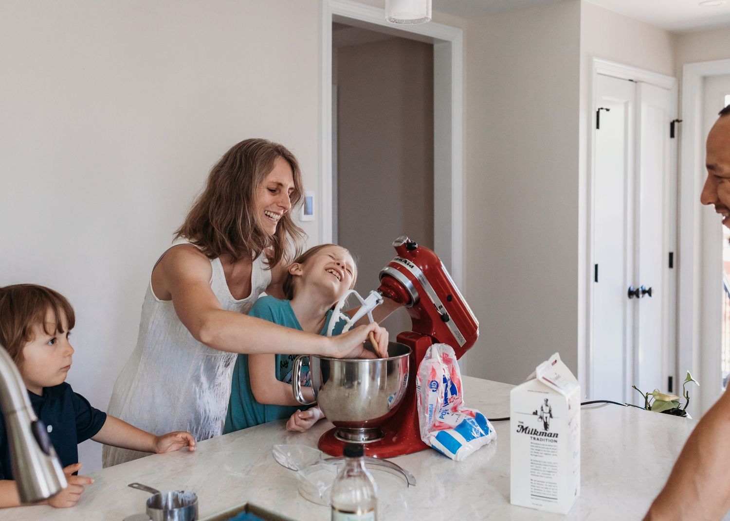 Family baking together in a bright kitchen with a red stand mixer on a marble countertop.
