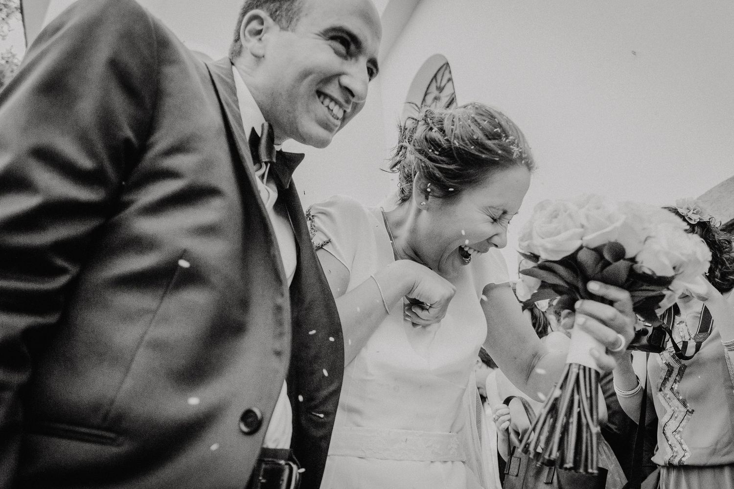 Bride in white gown walks down aisle with older woman in pink suit during indoor wedding ceremony.