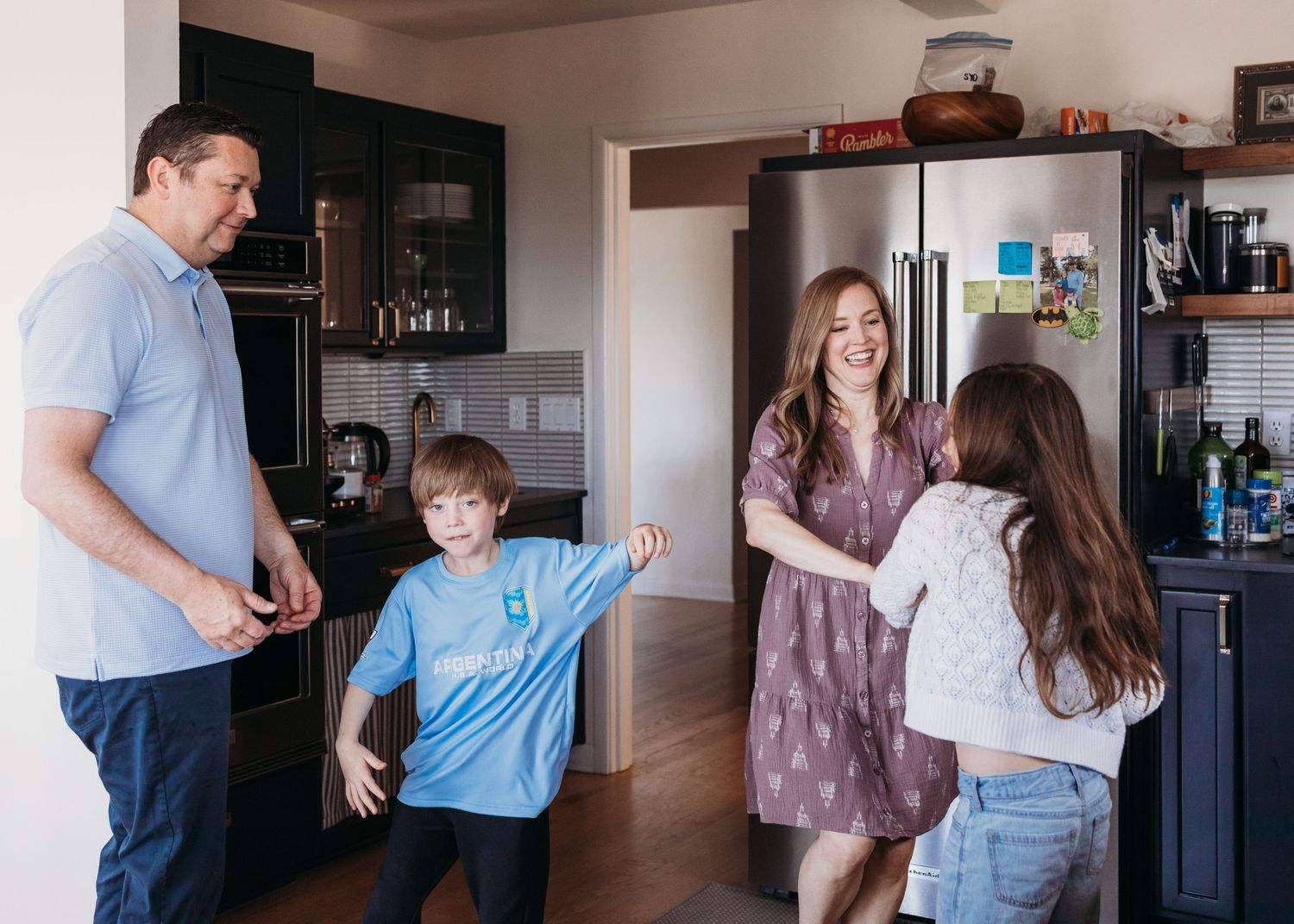 Family of four laughing and dancing together in a modern kitchen, creating joyful memories at home.