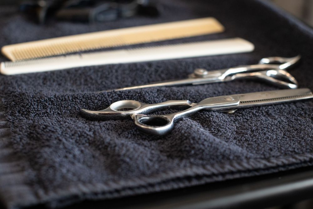 Professional barber scissors and comb laid on a black towel, essential hairdressing tools for precision haircuts.