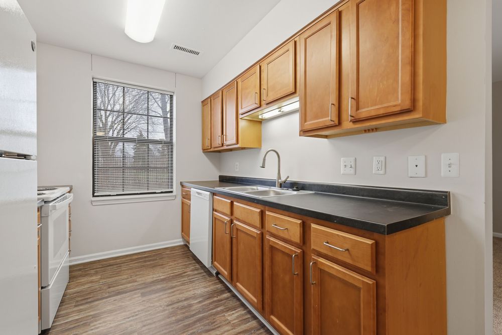 Modern kitchen with honey oak cabinets, dark countertops, stainless sink, and hardwood floors near bright window. Detroit MI