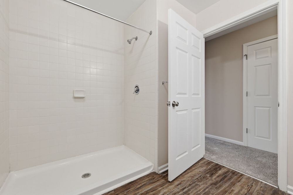 Clean white bathroom featuring tiled walk-in shower, hardwood floors, and open door to adjacent room. Detroit MI