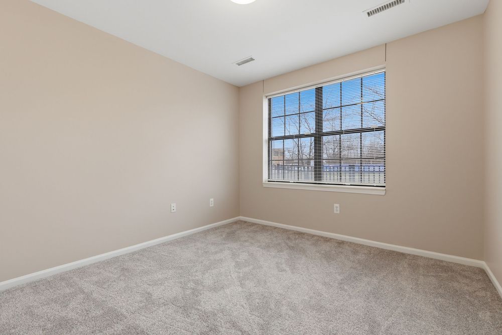 Empty bedroom with beige carpet, neutral walls, and a large window offering natural light in a modern home. Detroit MI