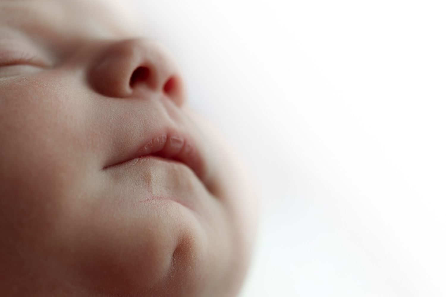 Peaceful newborn baby sleeping curled in a white bowl, wearing a delicate floral headband on a soft lace backdrop.