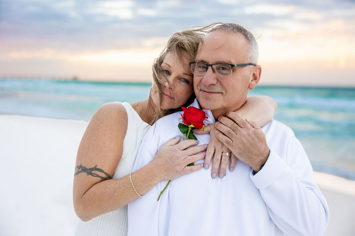 Couple in matching blue outfits sharing a romantic moment on a sandy beach with ocean waves behind them.