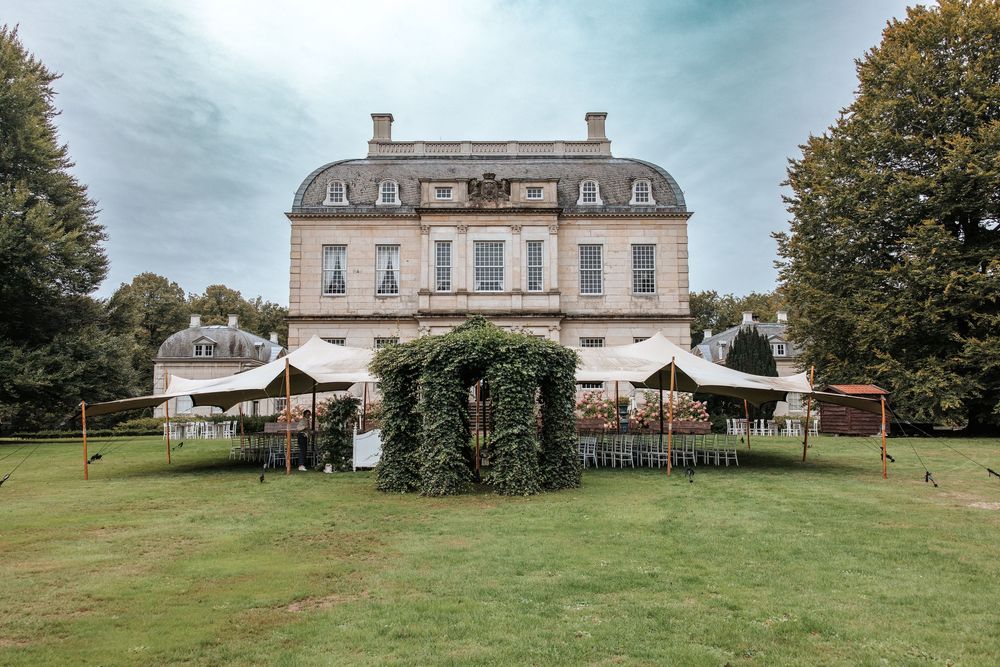 Elegant French-style manor house in the Netherlands, Landgoed van Voorst with ivy-covered gazebo and white marquee tents on lush green lawn.