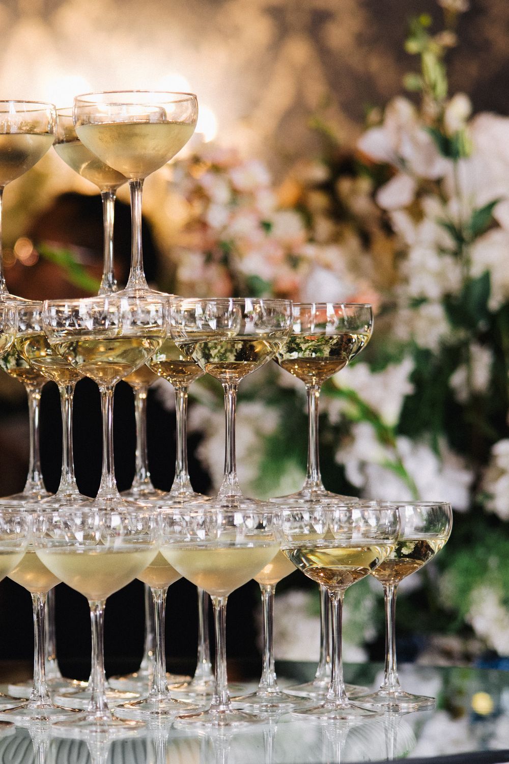 Elegant champagne tower with coupe glasses filled with sparkling wine at a wedding reception with floral decor.