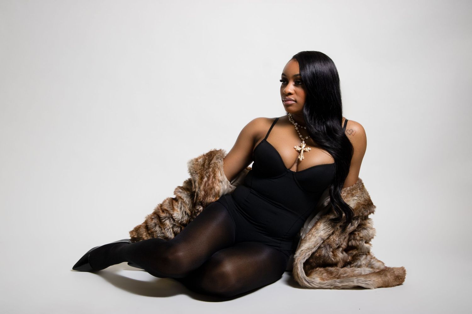 Woman in black dress and fur coat poses on studio floor.