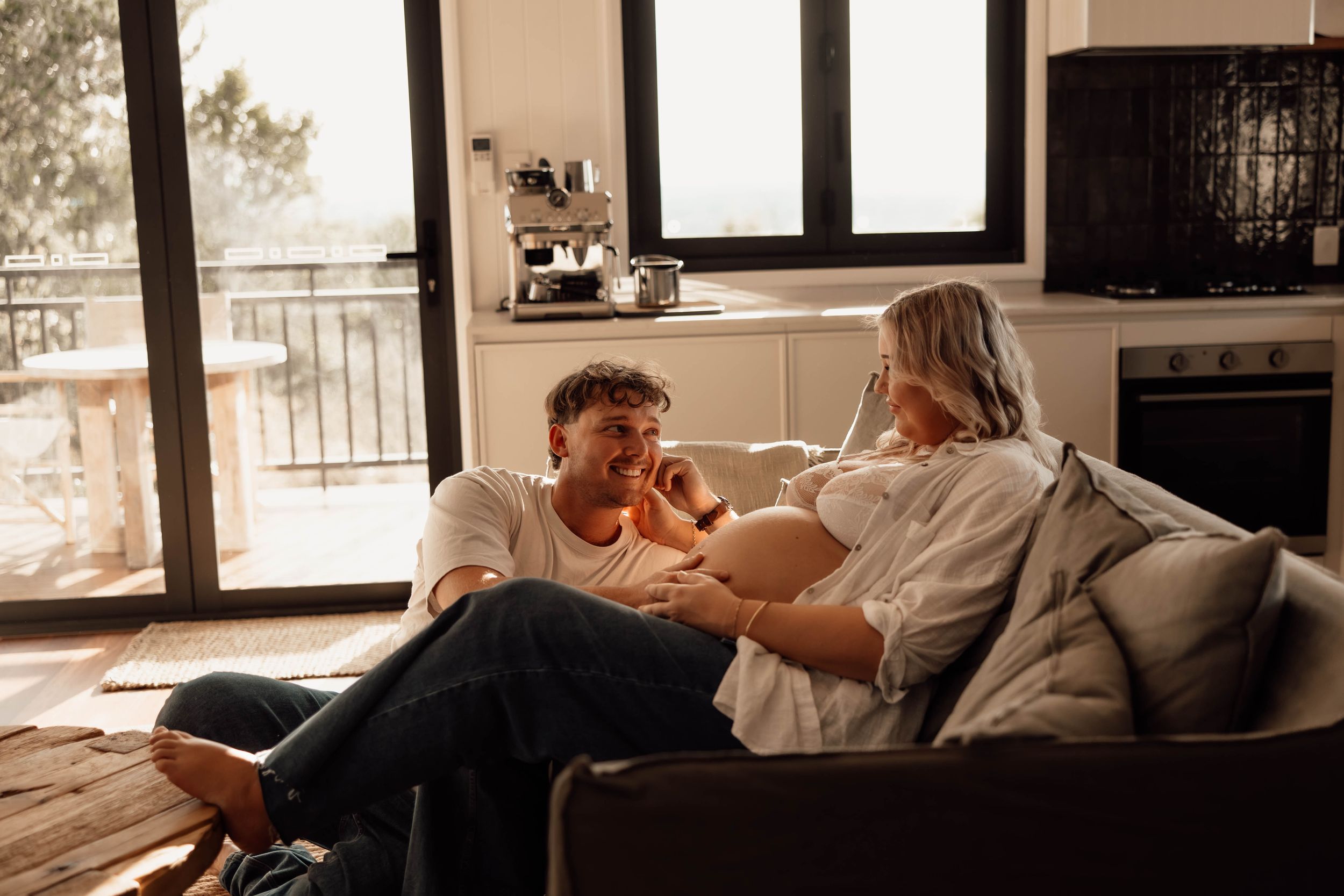 Couple relaxing together on a couch at home, sharing an intimate conversation in a cozy sunlit living room.
