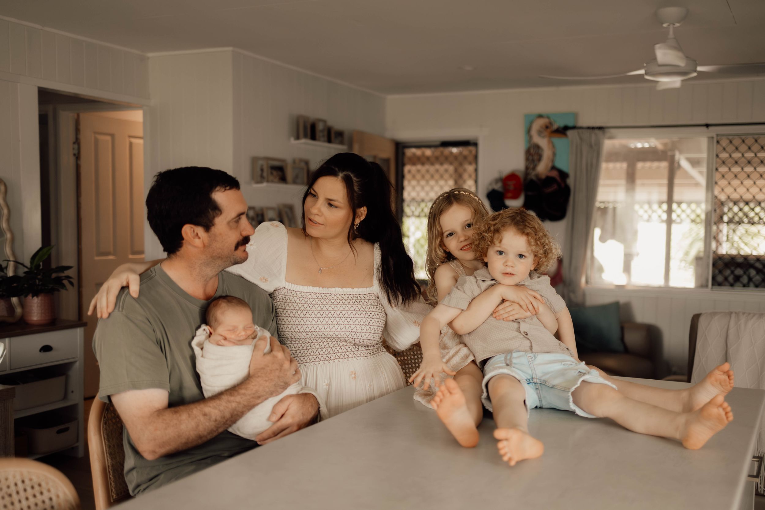 Happy family of five with newborn baby gathered around kitchen counter in bright home interior.